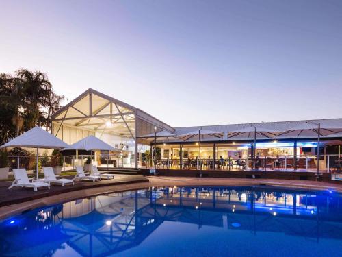 a swimming pool with chairs and a building at Mercure Townsville in Townsville