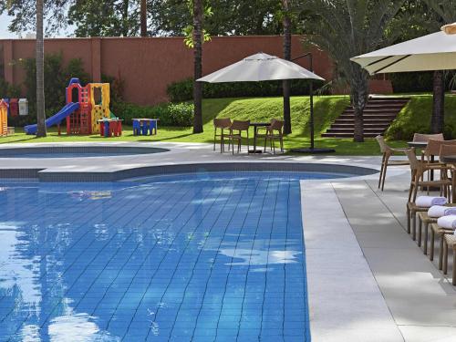 a swimming pool with tables and chairs and a playground at Novotel Campo Grande in Campo Grande