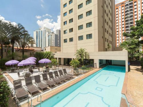 サンパウロにあるMercure São Paulo Ibirapuera Privilegeの椅子とパラソルのあるホテルのプールの眺め