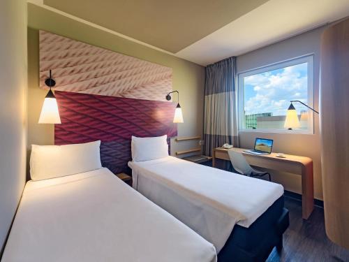 a hotel room with two beds and a desk and a window at ibis Ribeirao Preto Shopping in Ribeirão Preto