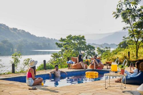 a group of people sitting around a swimming pool at Gram's at Shivom, Pawna Lake by StayVista in Lonavala