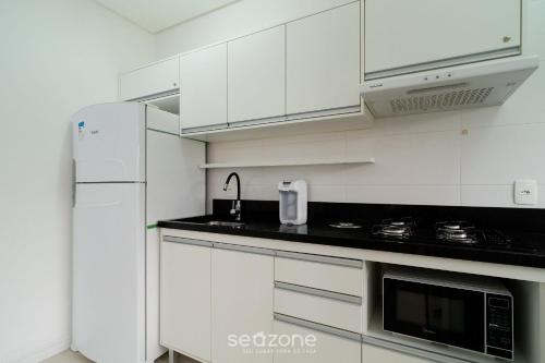 cocina blanca con armarios blancos y nevera en Apartamentos completos en edificio con piscina a 850m de la playa en el centro de Floripa - RIIs, en Florianópolis
