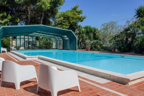 a swimming pool with white chairs and a green canopy at La Serra - Villa De Bonis in San Cesario di Lecce