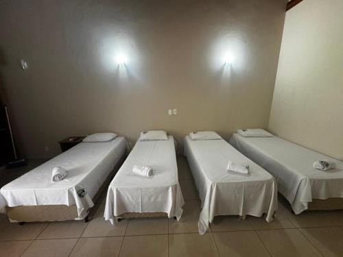 three beds in a room with white sheets at Hotel Fazenda Haras RD in Olímpia