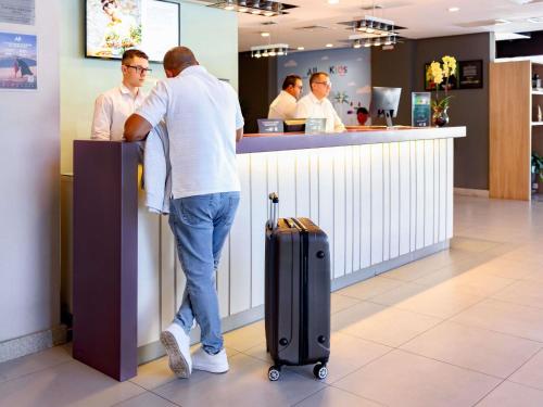 a man standing at a counter with his luggage at Mercure Florianópolis in Florianópolis