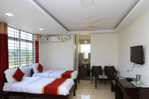 a hotel room with two beds and a desk and a tv at Hotel O Sri Sai Residency in Bidadi
