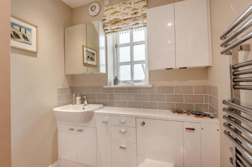 a white bathroom with a sink and a window at Dune House in Brancaster