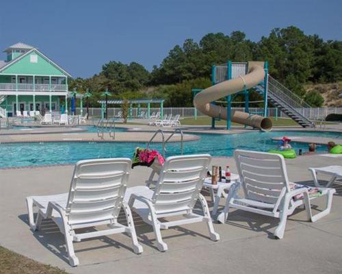 a little girl is sitting inbetween two chairs at a pool at BB47 - A Wave From It All in Croatan Shores