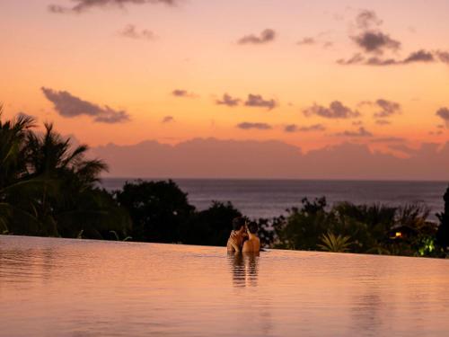 Una mujer sentada en la piscina infinita al atardecer en Pullman Bali Legian Beach, en Legian