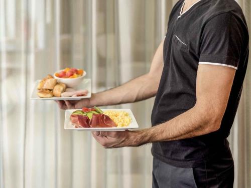 a man is holding two plates of food at ibis Esch Belval in Esch-sur-Alzette
