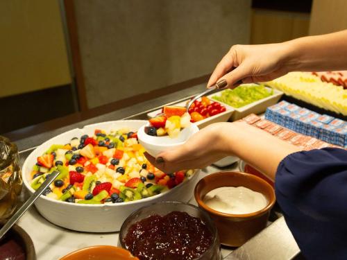 a person holding a spoon over a bowl of fruit salad at ibis Rio de Janeiro Barra da Tijuca in Rio de Janeiro