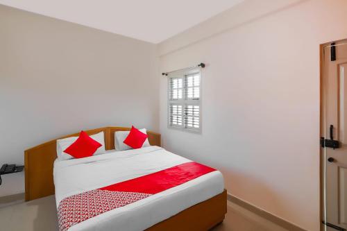 a bedroom with a bed with red pillows and a window at Hotel O Narayani Residency in Mysore