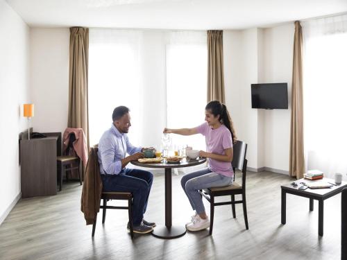 un hombre y una mujer sentados en una mesa en una habitación en Aparthotel Adagio Access Orléans, en Orléans