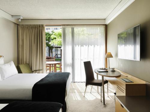 a hotel room with a bed and a desk and a table at Novotel Queenstown Lakeside in Queenstown