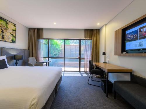 a hotel room with a bed and a desk and a tv at Mercure Penrith in Penrith