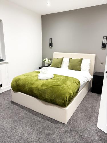 Un dormitorio con una gran cama blanca con una manta verde. en The Aurora Apartments, en Peterborough