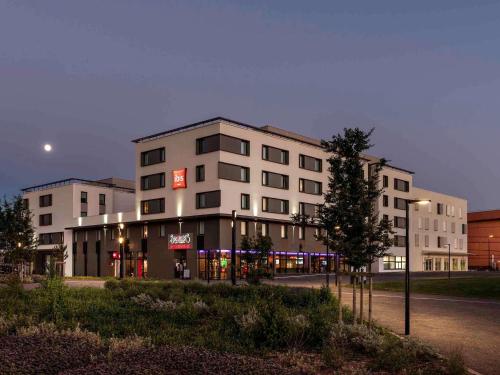 a large white building on the side of a street at ibis Saint Quentin en Yvelines - Vélodrome in Montigny-le-Bretonneux