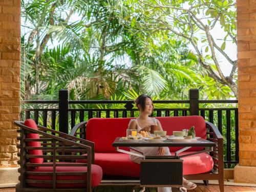 a woman sitting in a red chair at a table at Pullman Phuket Panwa Beach Resort in Panwa Beach