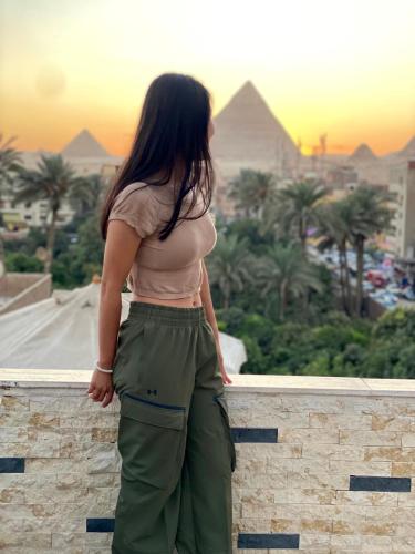 a woman standing on a wall looking at the pyramids at Pyramids Night Hotel &Free pickup shuttle in Giza