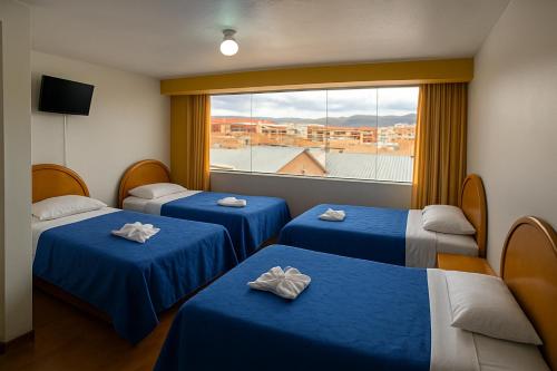プーノにあるHOSTAL ACUARIUS PUNOのベッド3台(青いシーツ付)、窓が備わる客室です。