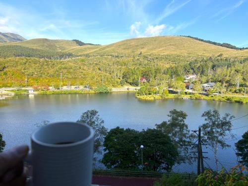 a person holding a cup of coffee looking at a lake at Fun & View Liitle Stay WAKUWAKU-BASE 白樺湖 in Chino