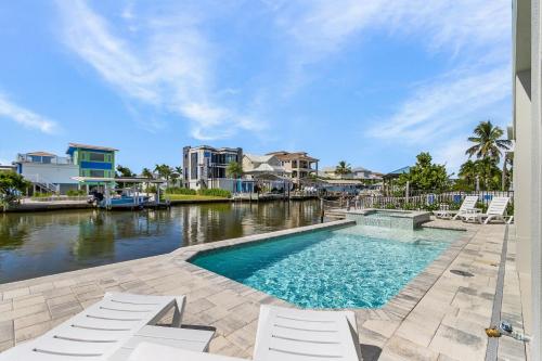 a swimming pool with white chairs next to a river at Brand New Luxury Build 265 Carolina Ave- Heated Pool, Hot Tub home in Fort Myers Beach