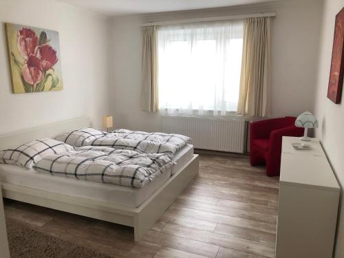 a bedroom with a bed and a red chair and a window at Wulfenia Apartments in Hermagor