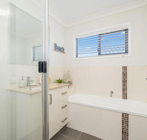 a white bathroom with a tub and a sink at The Lazy Tide in Burrum Heads
