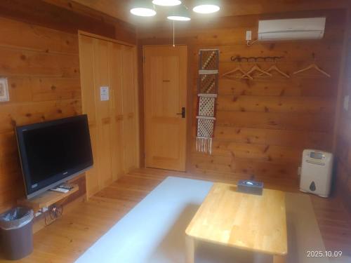 a living room with a television and a wooden wall at 大室山の麓ログハウスすくすく in Ito