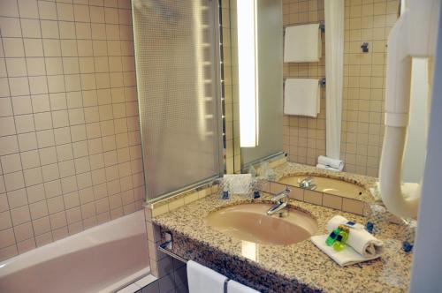 ein Badezimmer mit einem Waschbecken, einer Badewanne und einem Spiegel in der Unterkunft Novotel Andorra in Andorra la Vella