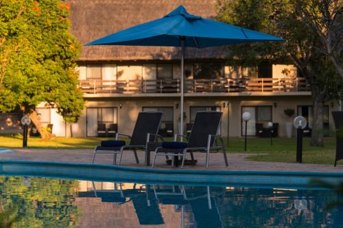a blue umbrella and chairs next to a swimming pool at Azambezi River Lodge in Victoria Falls