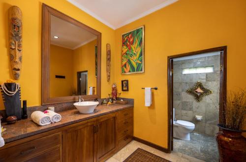 a yellow bathroom with a sink and a toilet at Villa Air Terjun Bucuan in Sukawati
