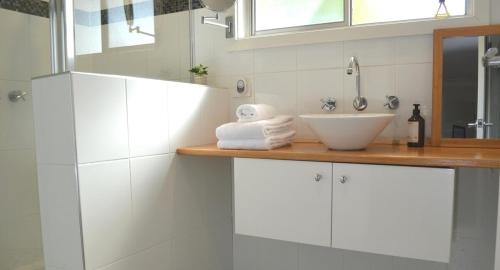 ein weißes Badezimmer mit Waschbecken und Spiegel in der Unterkunft Classic Meets Contemporary 1960's Beach House in Malua Bay