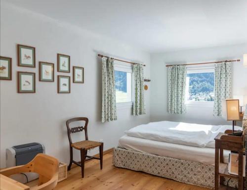 een slaapkamer met een bed en een stoel en 2 ramen bij Chesa Saura in Ponte