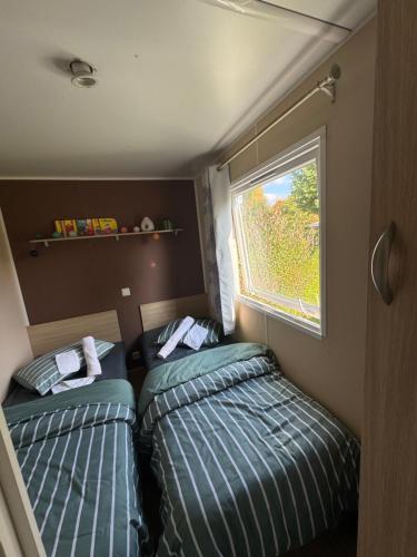 two beds in a small room with a window at Mobilhome Évasion Fun Activités, détente et nature aux Fontaines in Ivry-la-Bataille