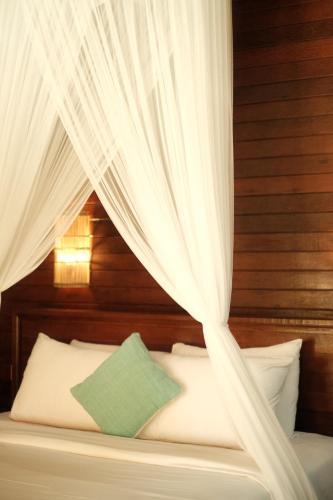 un lit avec des rideaux blancs et un oreiller vert dans l'établissement Alinn Villas, à Nusa Lembongan