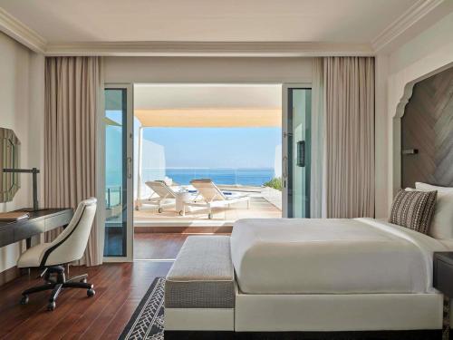 a bedroom with a bed and a desk and a balcony at Fairmont Fujairah Beach Resort in Al Aqah
