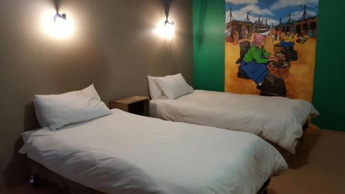 two beds in a room with a painting on the wall at The Backpack Shack in Mossel Bay