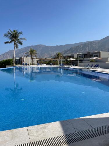 a large blue swimming pool with palm trees and buildings at Sunrise Haven in As Sīfah