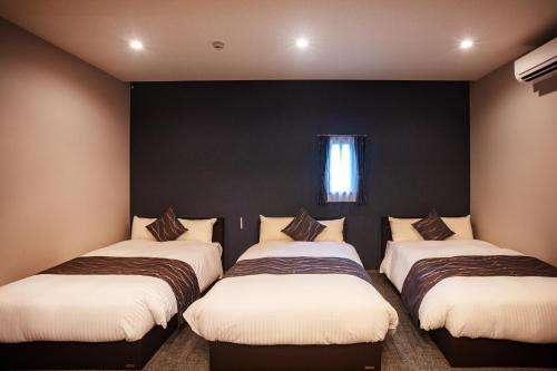 three beds in a room with black walls and a window at Grand Inn Hakata in Fukuoka