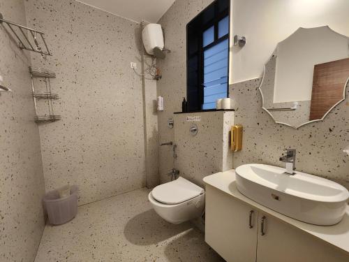 a bathroom with a toilet and a sink and a mirror at Bright Candolim 1BHK with Pool, Gym, Parking - 5 Minutes to Beach in Candolim