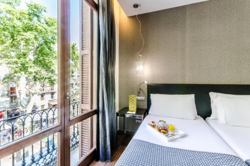 a bed with a tray of food on it next to a window at Exe Ramblas Boquería in Barcelona