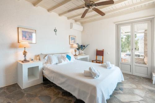 a white bedroom with a bed and a ceiling fan at Villa Néréides in Koundouros