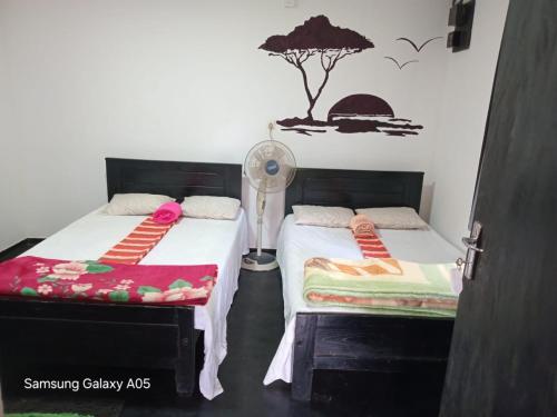 a bedroom with two beds with a fan and a tree on the wall at Ella Cool Air Cabana in Ella