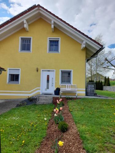 une maison jaune avec un banc dans la cour dans l'établissement Ferienhaus Fuchs, à Neukirchen vorm Wald