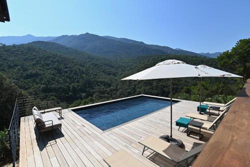 a swimming pool with an umbrella and chairs and a deck at Casa Paula in Serriera