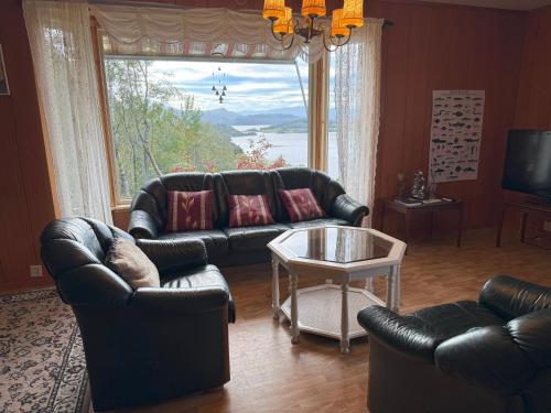 a living room with leather furniture and a large window at Landlig hus på kysten in Tustna