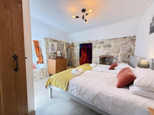 a bedroom with two beds and a stone wall at Sixpence Cottage, a few steps from the harbour! in St Ives