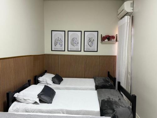 two beds in a room with three pictures on the wall at Casa climatizada a 10 min do AEROPORTO in Várzea Grande