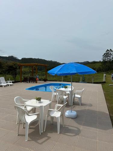 a table and chairs with a blue umbrella next to a pool at Morada do Campo in Biguaçu